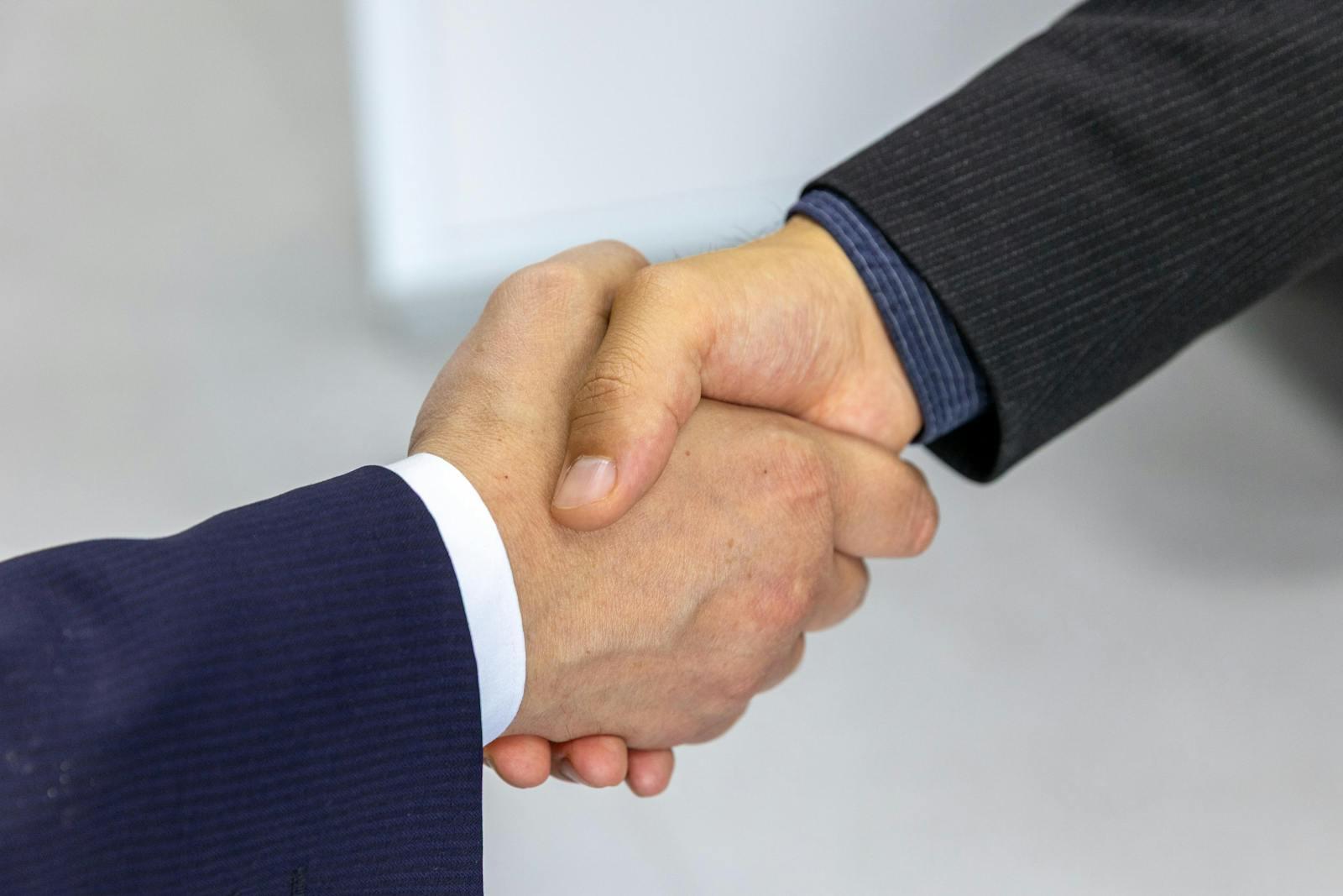 Two businesspeople in suits shaking hands close-up.