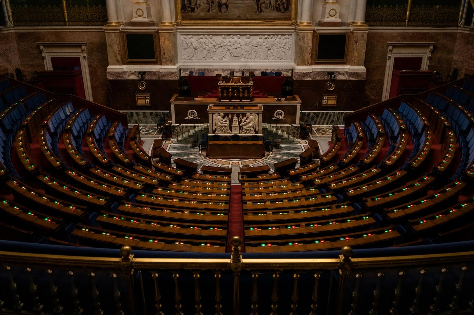 Empty blue benches and voting consoles inside the French National Assembly.