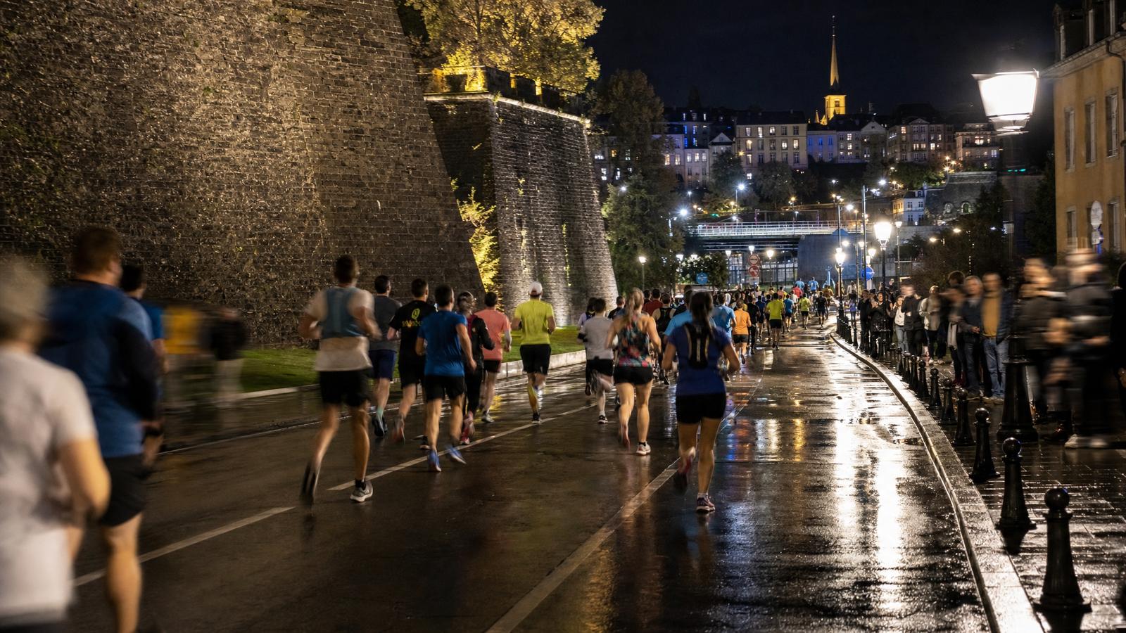 Night runners on wet Luxembourg City streets during a marathon event.