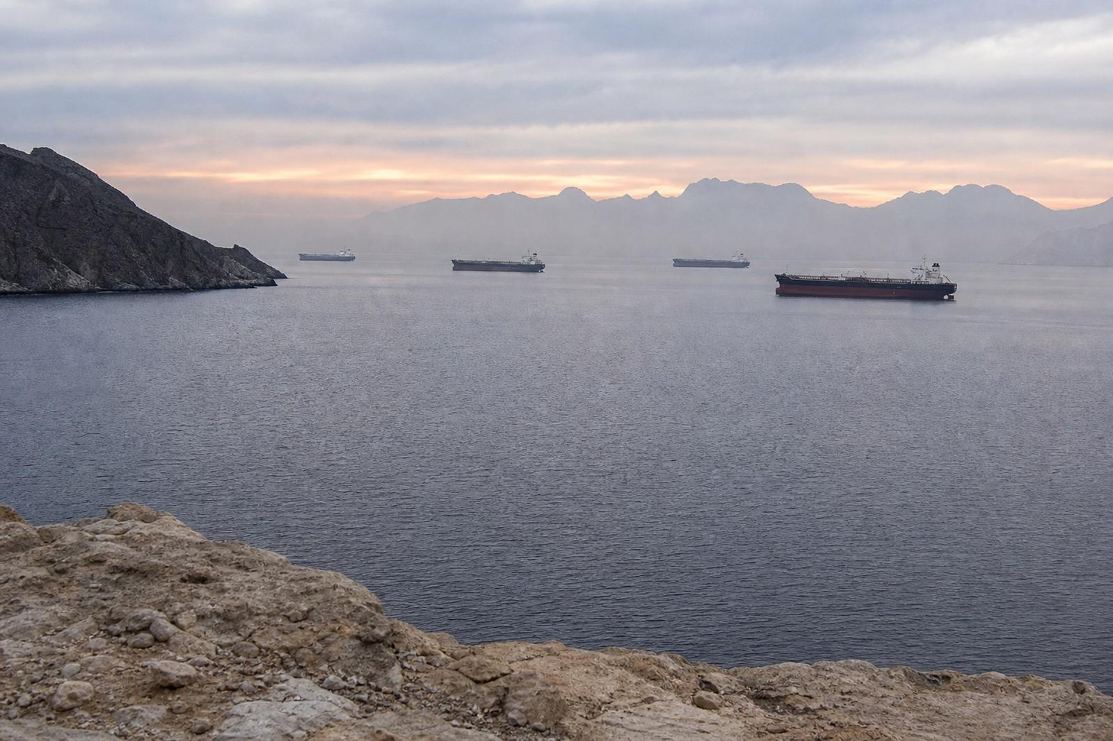 Oil tankers wait beyond an empty shipping lane in the Strait of Hormuz at dawn.