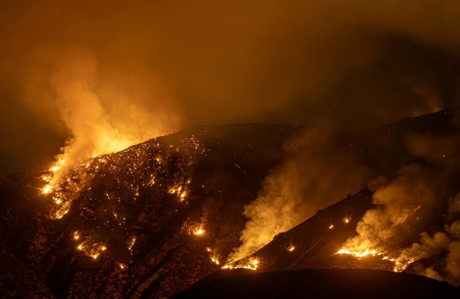 An intense wildfire blazes through mountains at night in California.